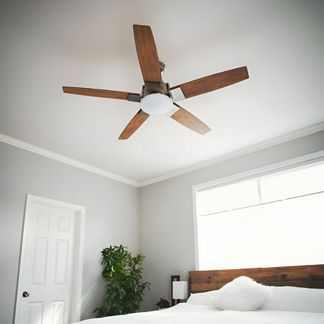 Ceiling fan with wooden blades above a bed in a modern, minimalist bedroom. The room has white walls, a large window, a plant, and a wooden headboard.