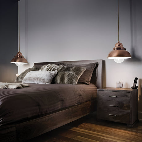 A modern bedroom with a wooden bed and gray bedding, flanked by two hanging pendant lamps. A wooden nightstand holds a clock and cordless phone. The room has a calm and minimalist design.