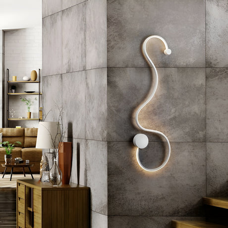A modern living room features a unique, curved wall lamp on a textured gray corner. The room includes a wooden cabinet with decor, a beige sofa, and shelves with plants, blending contemporary and cozy elements.