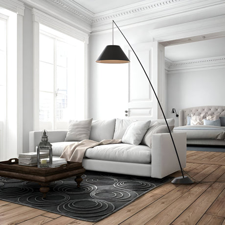 Modern living room with a white sofa, black arc floor lamp, and dark wooden coffee table on a circular patterned rug. The room has bright windows and an open doorway leads to a bedroom with a bed.