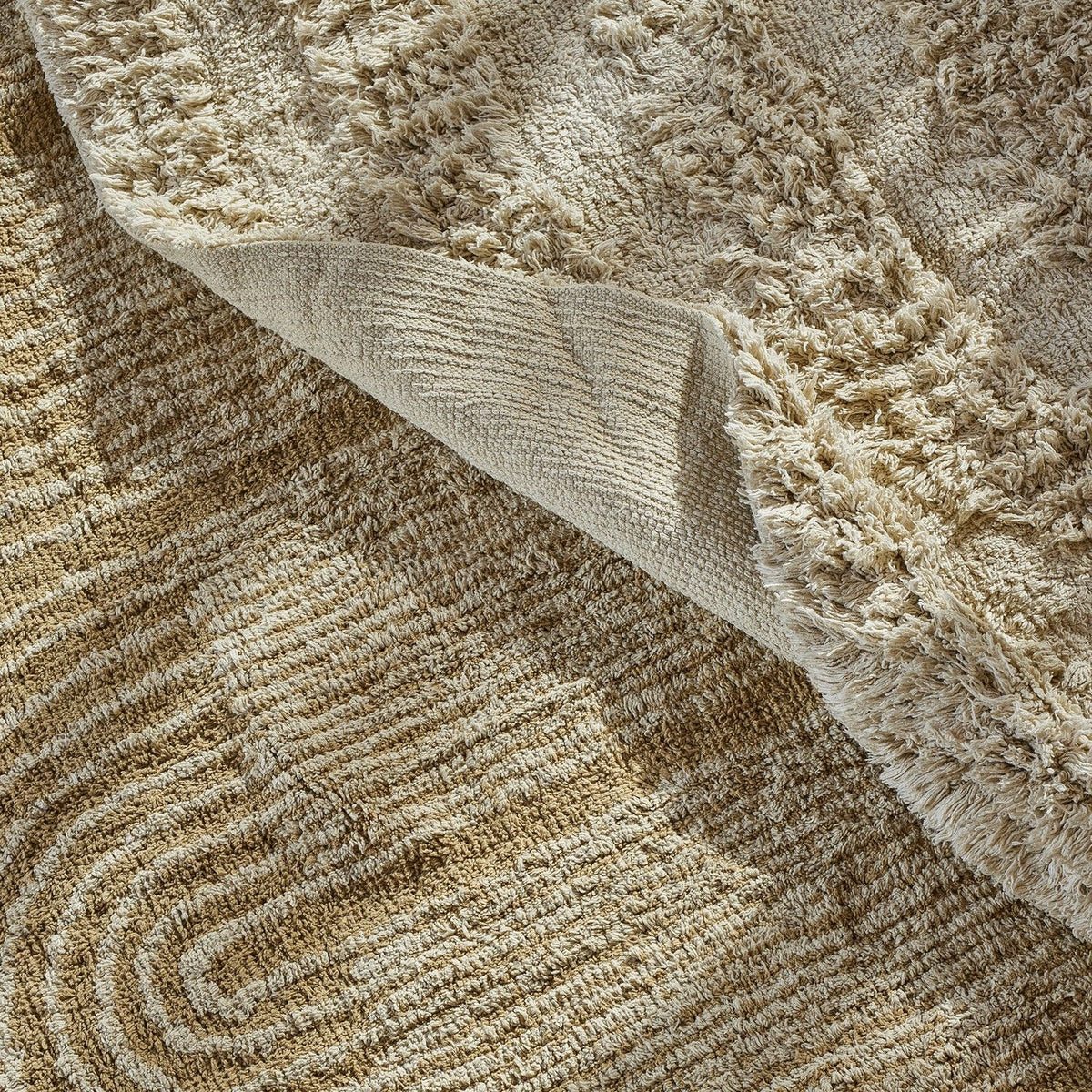Zeynep Cotton Rug 215x150cm in brown, shown folded back to reveal the woven backing and plush pile with a looped arch and striped pattern.