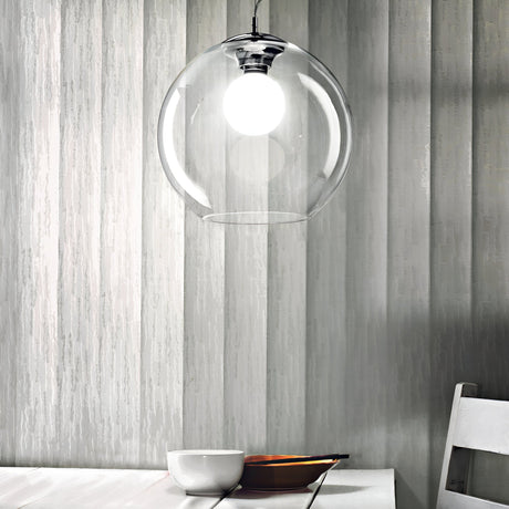 A minimalist dining setting features the Emberlyte 1 Light Glass Pendant in chrome, measuring 30cm, hanging over a wooden table with a white bowl and plate. The background showcases striped wallpaper panels in subtle grey tones.