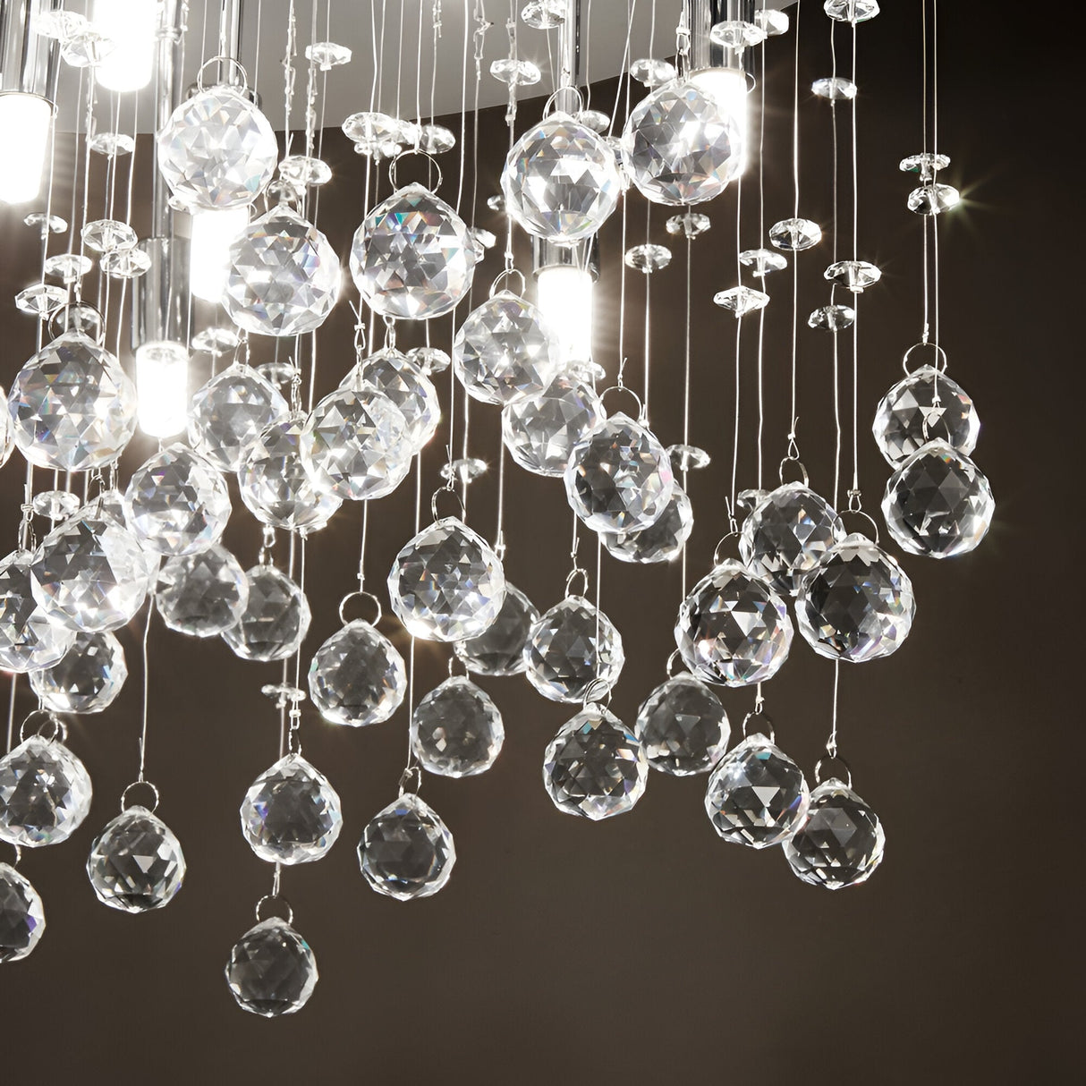 A cluster of sparkling crystal orbs hangs elegantly from a ceiling, similar to the Solisera 8 Light Crystal Semi Flush Chandelier - Chrome. Suspended by thin wires, these chrome-accented crystal pendants create a luxurious and intricate display against a dark background, reflecting light in every direction.