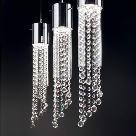 A trio of Cono 1 Light Glass Pendants in chrome, featuring sleek cylindrical designs and adorned with cascading crystal beads, illuminate a dark background with a gentle, luxurious glow.