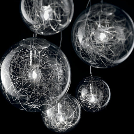 The Lyria 5 Light Cluster Pendant - Clear features five clear glass pendant lights set against a dark backdrop. Each spherical orb, encased with intricate metal wire detailing around the bulb, exemplifies modern design. These illuminated orbs serve as breathtaking blown glass diffusers, forming an artistic masterpiece.