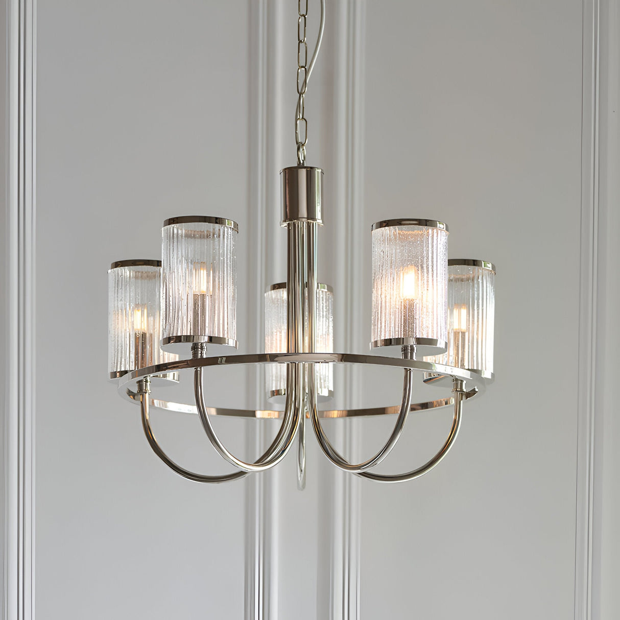Endon Brenfield 5 light nickel pendant with curved arms and ribbed bubble glass cylindrical shades, suspended from a chain against a pale panelled wall.
