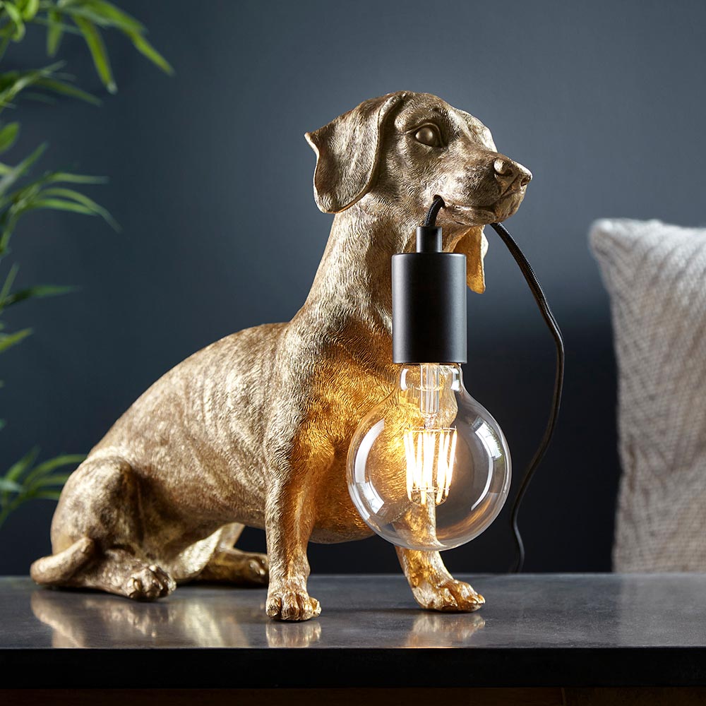 Bevworth Table Lamp in gold resin dachshund shape with matt black E27 holder and exposed globe bulb, shown on a dark table indoors.