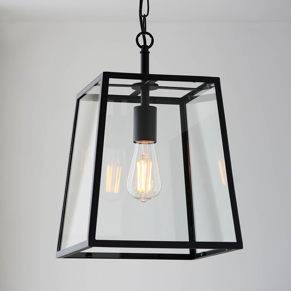 Brenton Lantern Pendant in black, a tapered box-frame ceiling light with clear glass panels and an exposed E27 filament bulb.