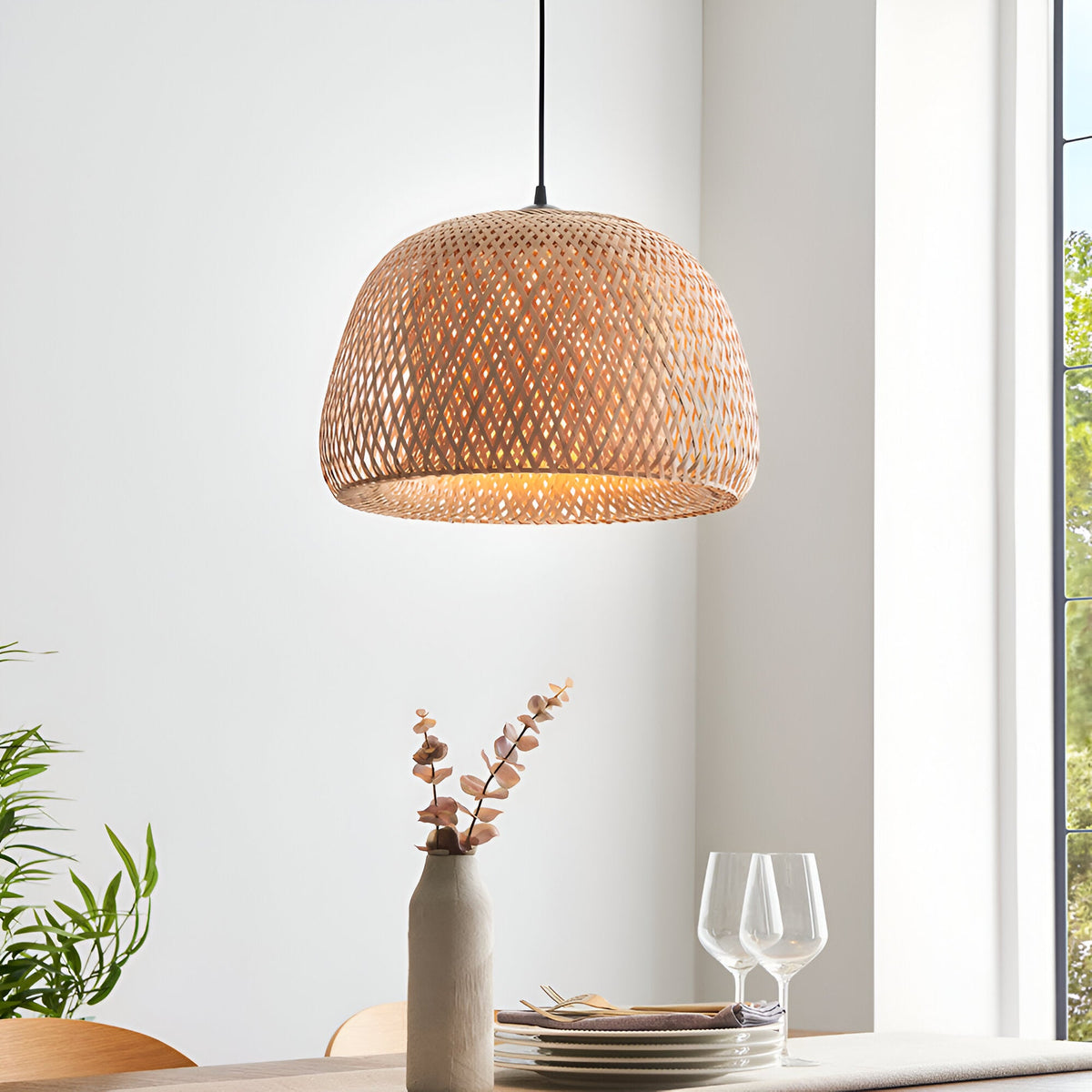 Aldstead Oval Pendant in Natural, a woven rattan dome shade with black cord, hung above a dining table in a bright room.