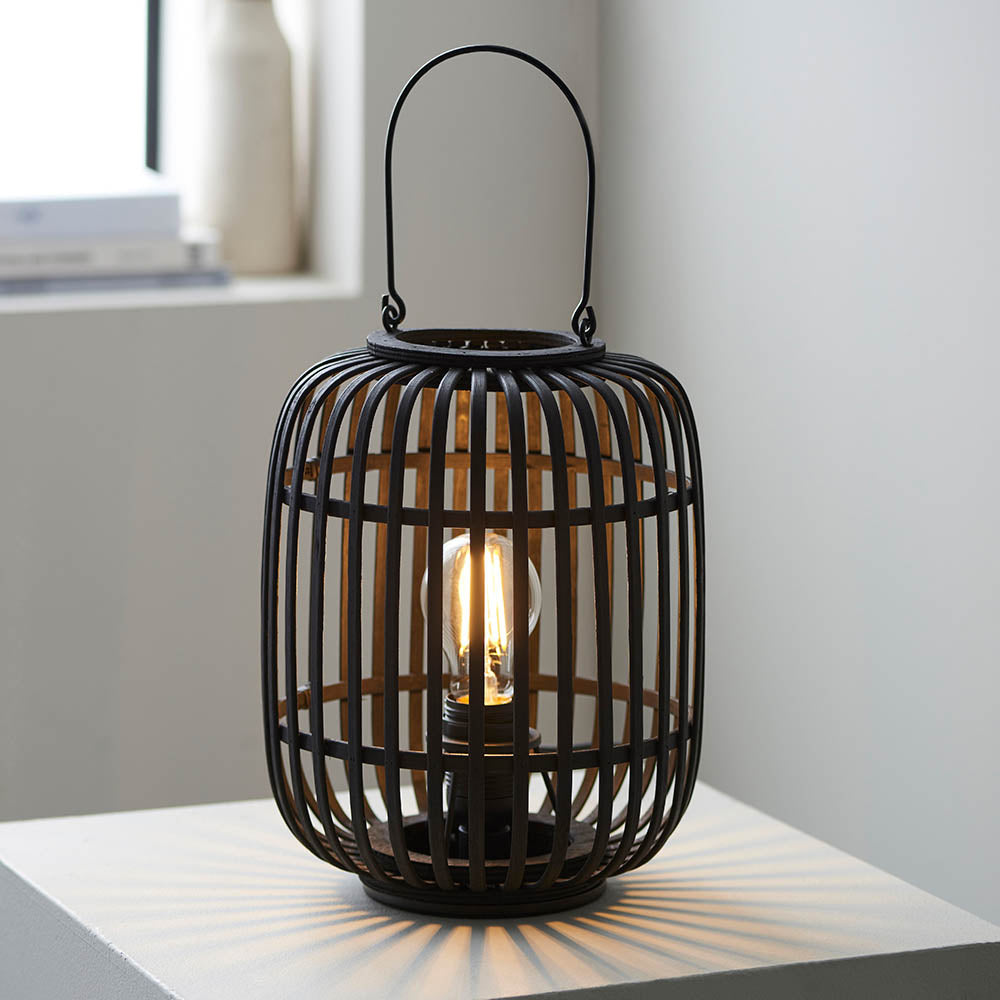 Endon Bracken table lamp in matt black with an open bamboo cage, arched handle and lit E27 filament bulb, shown on a white side table.