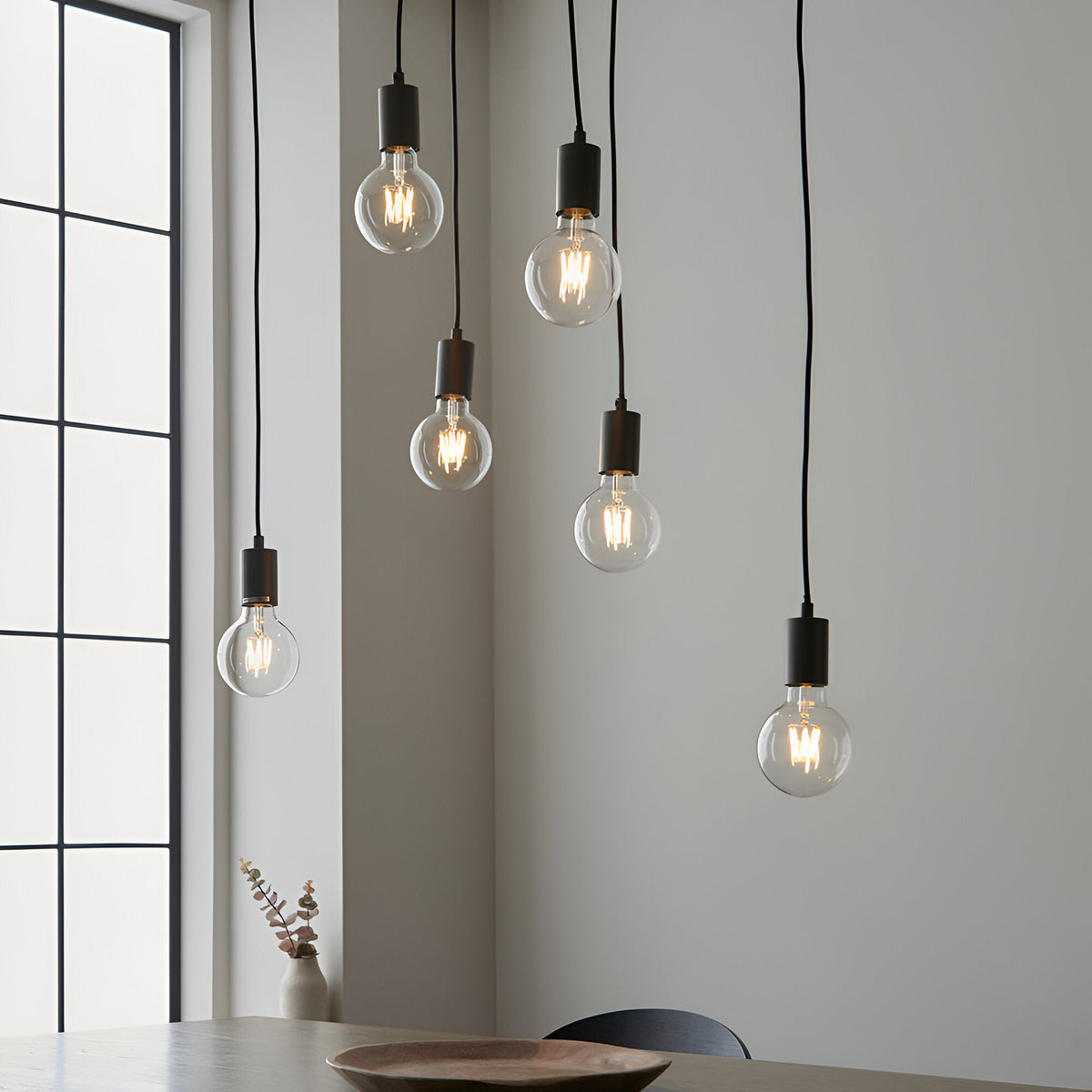 Endon Cliffwell 6 light cluster pendant with clear globe filament bulbs on black flexes and anthracite lampholders, above a dining table by a window.
