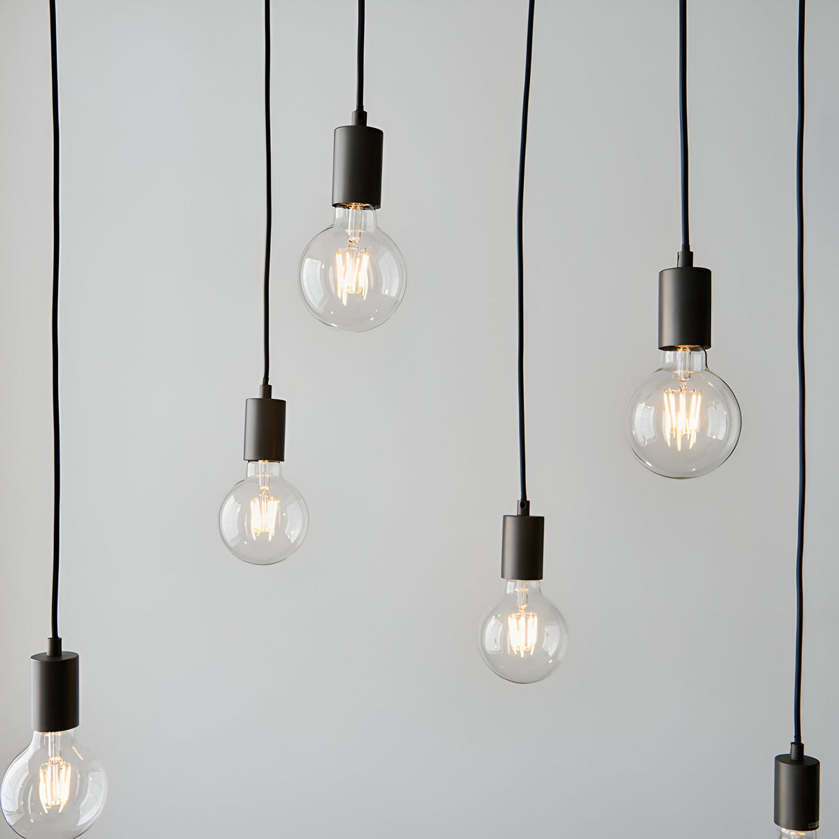 Endon Cliffwell pendant lights with six clear filament E27 globe bulbs on black flex cords and anthracite lampholders against a plain light grey background.