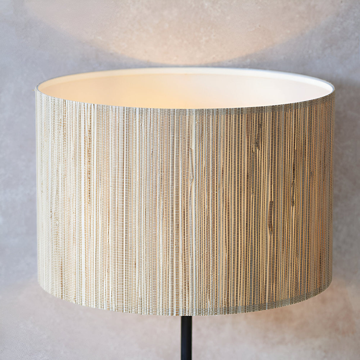 Endon Salcombe floor lamp close-up showing the woven natural seagrass drum shade lit with a warm glow above a slim matt black stem.