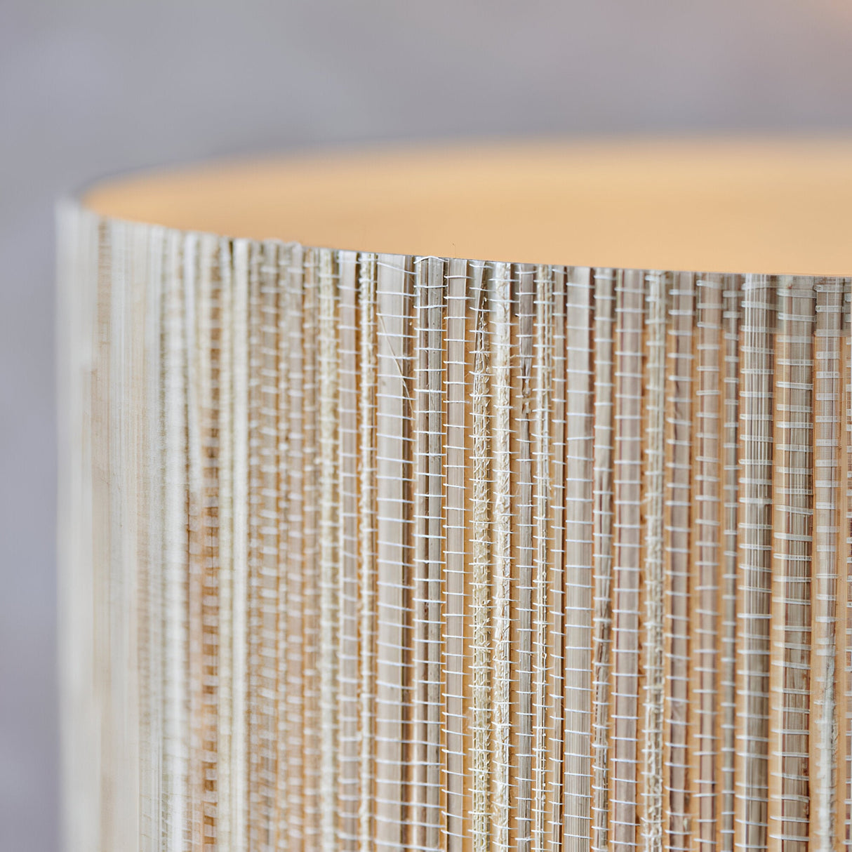 Close-up of the Endon Salcombe floor lamp's woven natural seagrass drum shade, showing vertical grain and stitching illuminated with a warm glow.