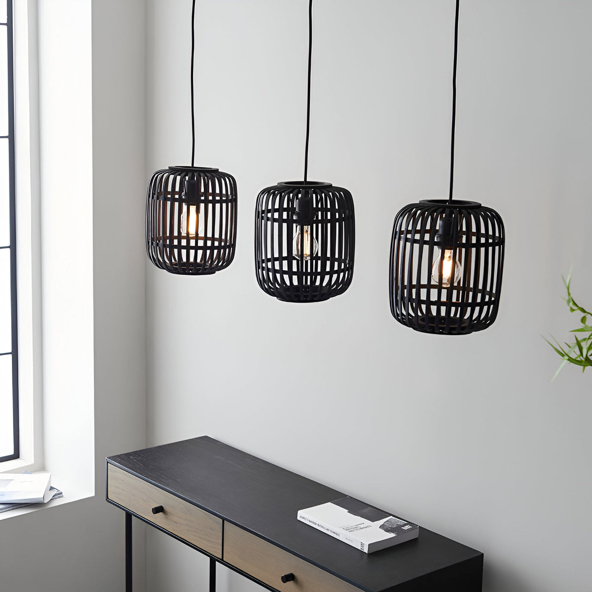 Endon Bracken 3 light pendant with matt black bamboo cage shades and E27 filament bulbs, hung above a dark console table in a bright living space.