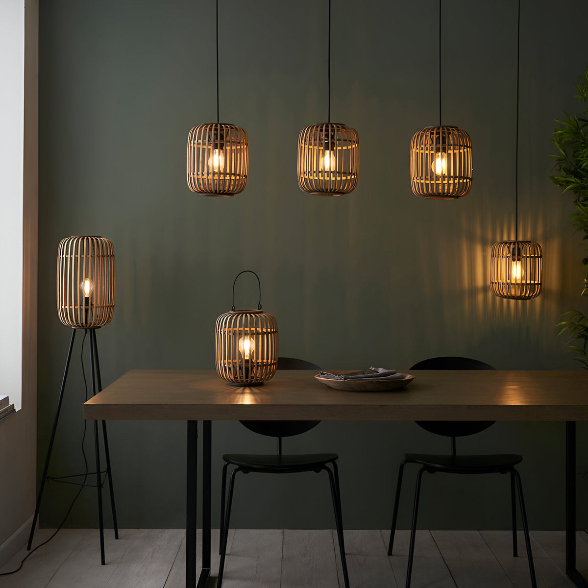 Endon Bracken table lamp with natural bamboo cage and filament bulb on a dining table, alongside matching pendant and floor lamps against a green wall.