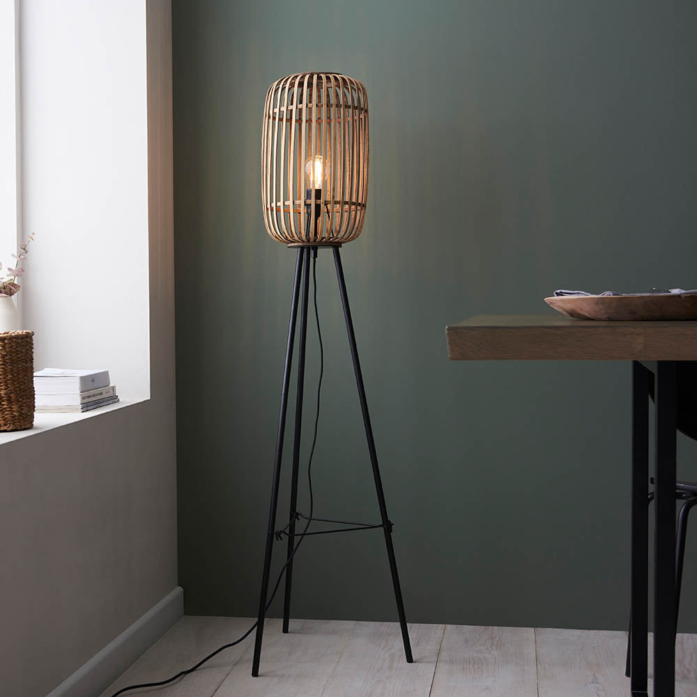 Bracken Floor Lamp in black and natural, with a bamboo cage shade on a matt black tripod base, shown lit in a living room setting.