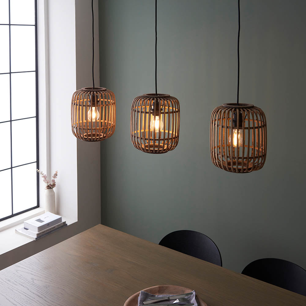 Endon Bracken 3 Light Pendant in black and natural bamboo, three cage shades with filament bulbs, hung above a wooden dining table by a green wall.