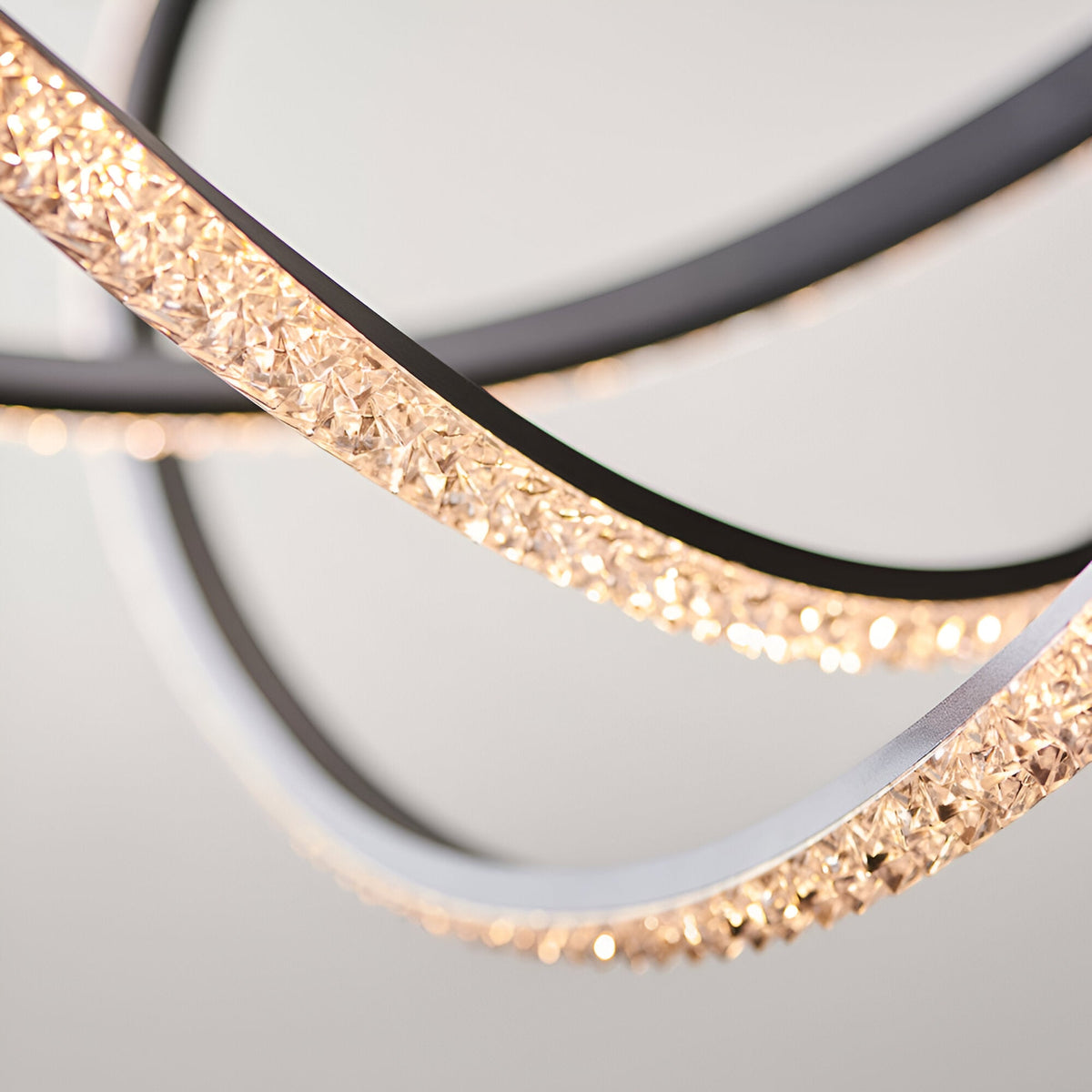 Close-up of the Bramcombe Pendant with curved matt black rings and faceted acrylic crystal detail lit warm white, against a plain light grey background.