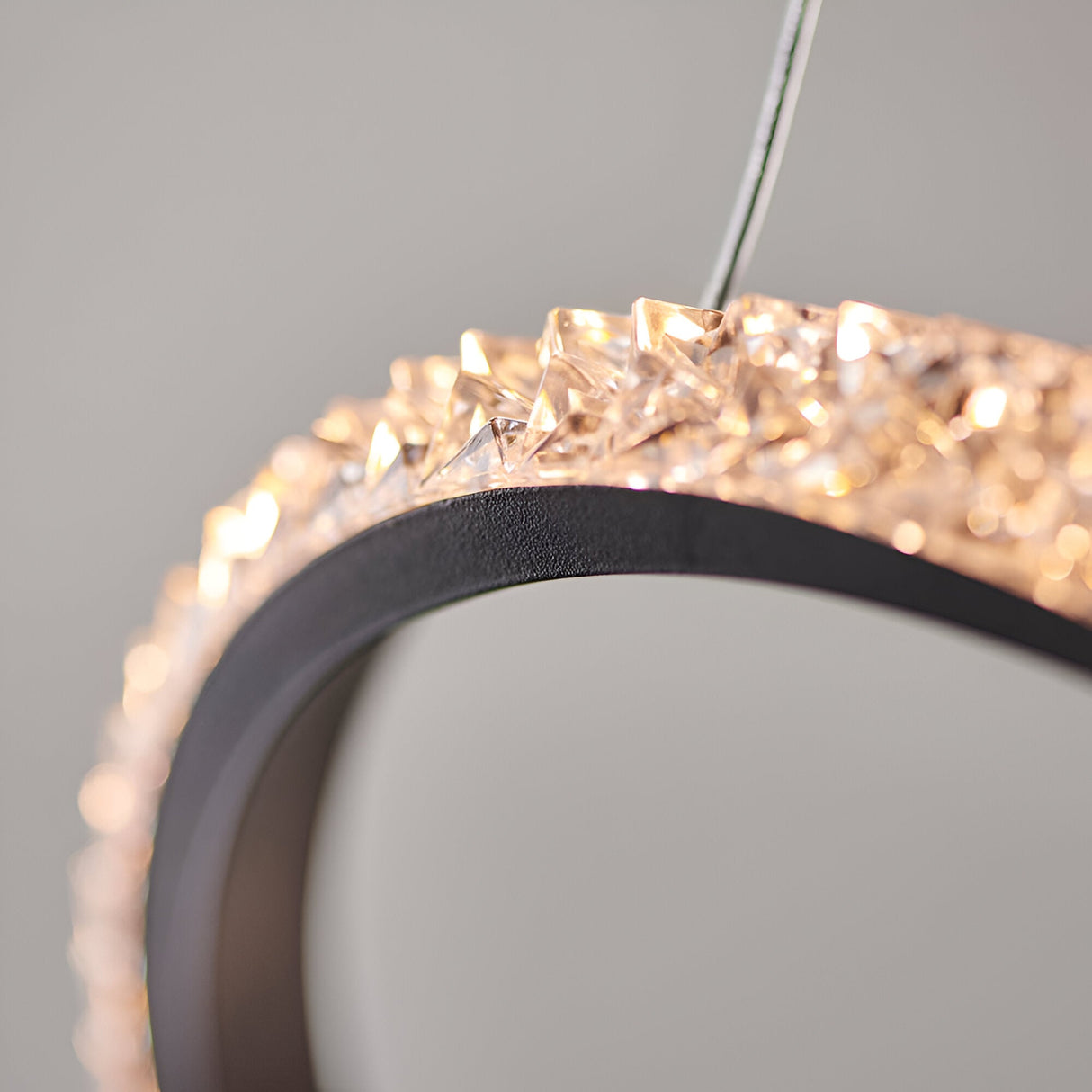 Close-up of the Bramcombe Pendant in matt black with faceted clear acrylic detail catching illuminated light, shown against a plain grey background.