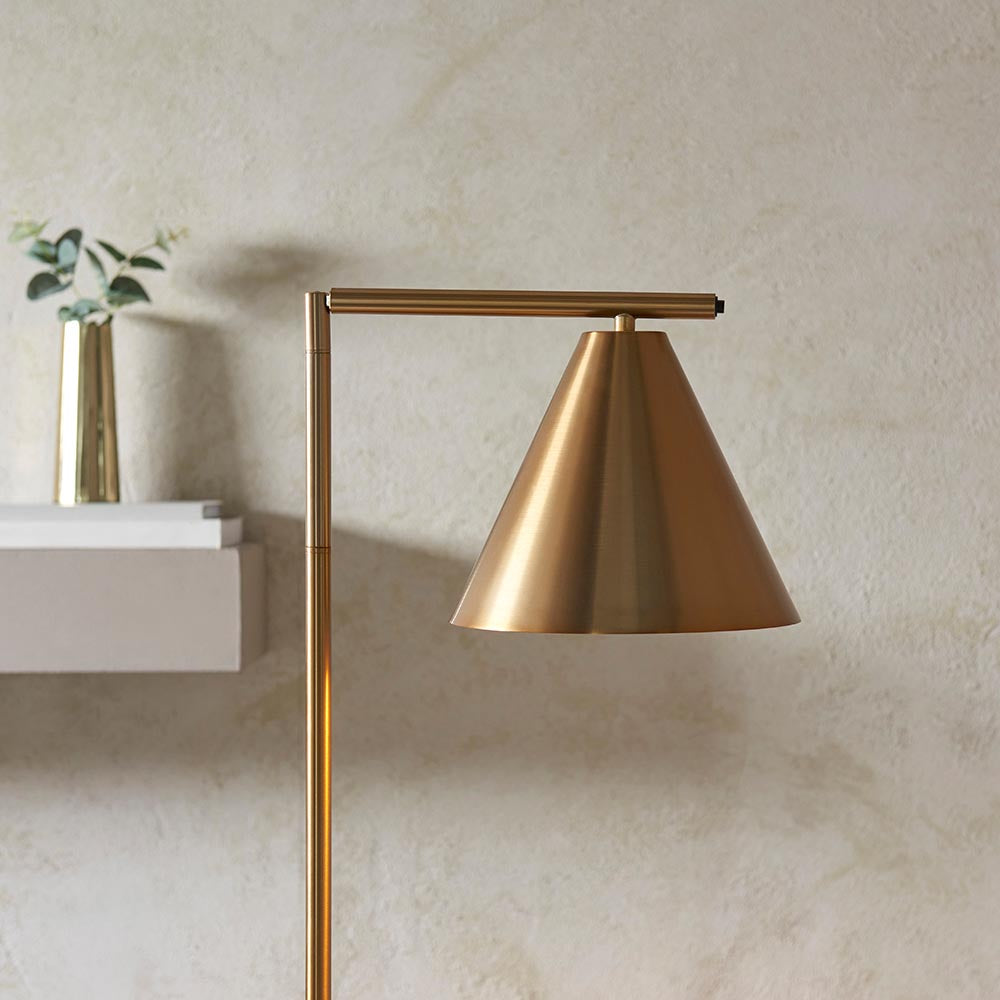 Endon Ashworth floor lamp in antique brass, showing the adjustable arm and conical shade angled beside a wall-mounted shelf with a brass vase.