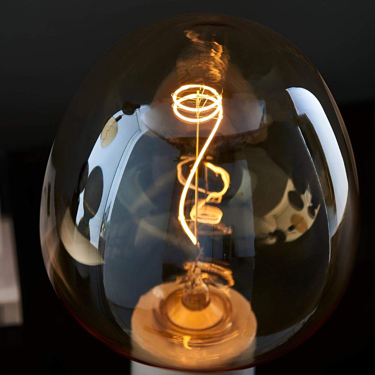 Endon 4W E27 LED filament swirl bulb illuminated in warm amber, showing the curved filament through tinted glass against a dark background.