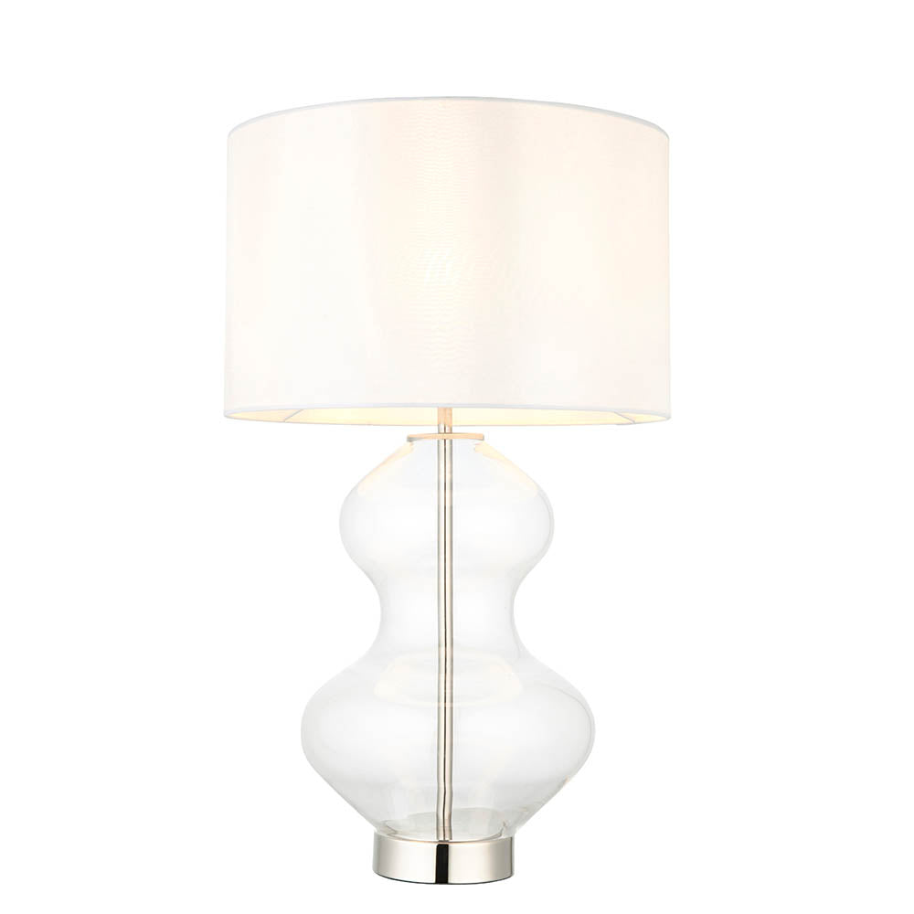 Endon Brockley table lamp with a clear glass hourglass base, polished nickel metalwork and vintage white fabric drum shade on a plain background.