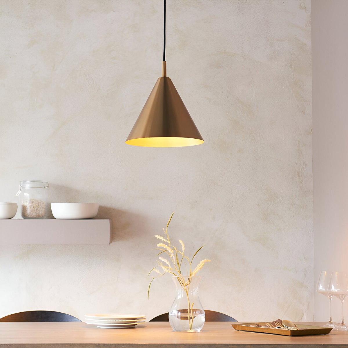 Ashworth Pendant in brass with cone-shaped metal shade, hung above a dining table in a neutral, minimalist room setting.