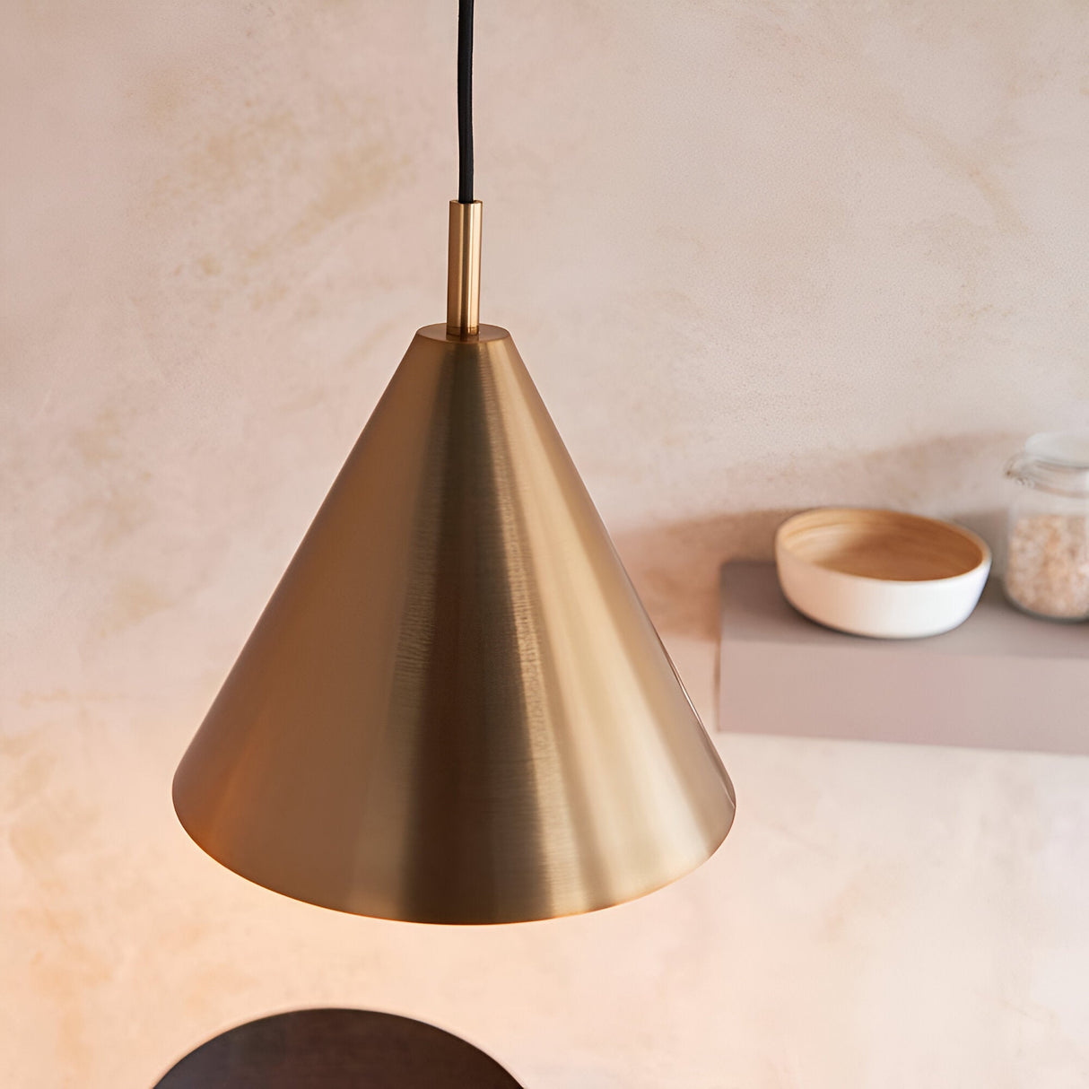 Ashworth Pendant in brass, a single cone-shaped shade with matching painted interior, hung above a shelf styled with bowls in a neutral kitchen setting.