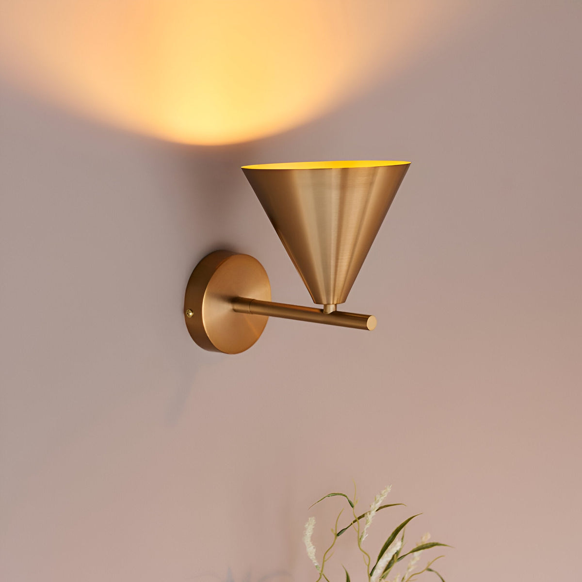 Endon Ashworth brass wall light with a conical shade on an adjustable arm, casting a warm glow on the wall above.