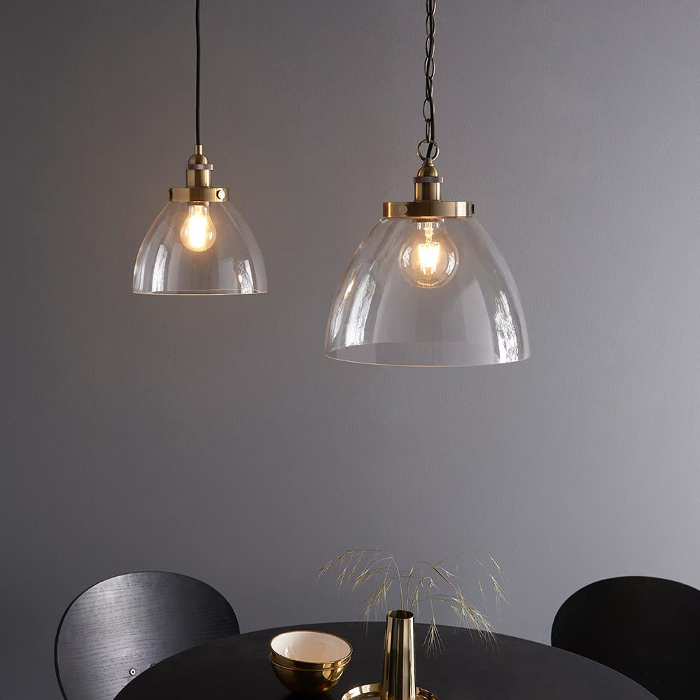 Wentworth Pendant in brass with clear glass dome shade and visible filament bulb, shown with a matching smaller pendant above a dark dining table.