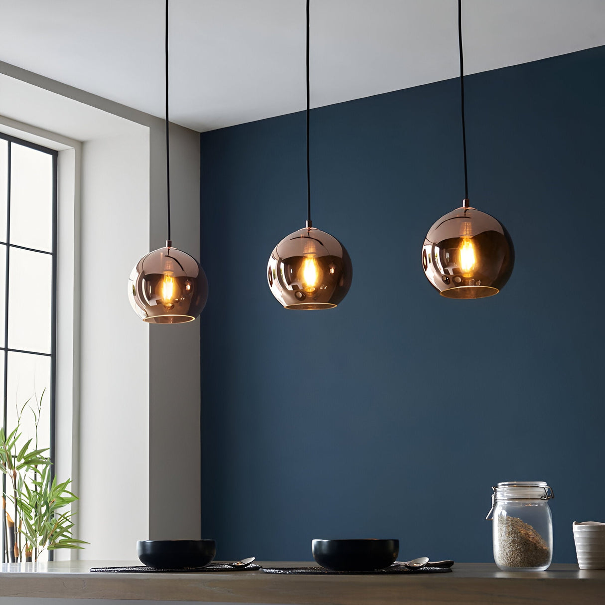 Endon Ashbourne 3 light linear pendant with copper mirrored glass globes on black cables, illuminated above a kitchen counter against a deep blue wall.