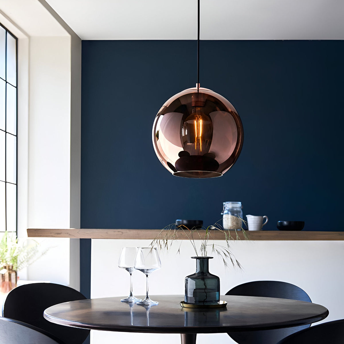 Endon Ashbourne pendant with a single copper mirrored glass globe shade and black cable, hung above a round dining table against a deep blue wall.