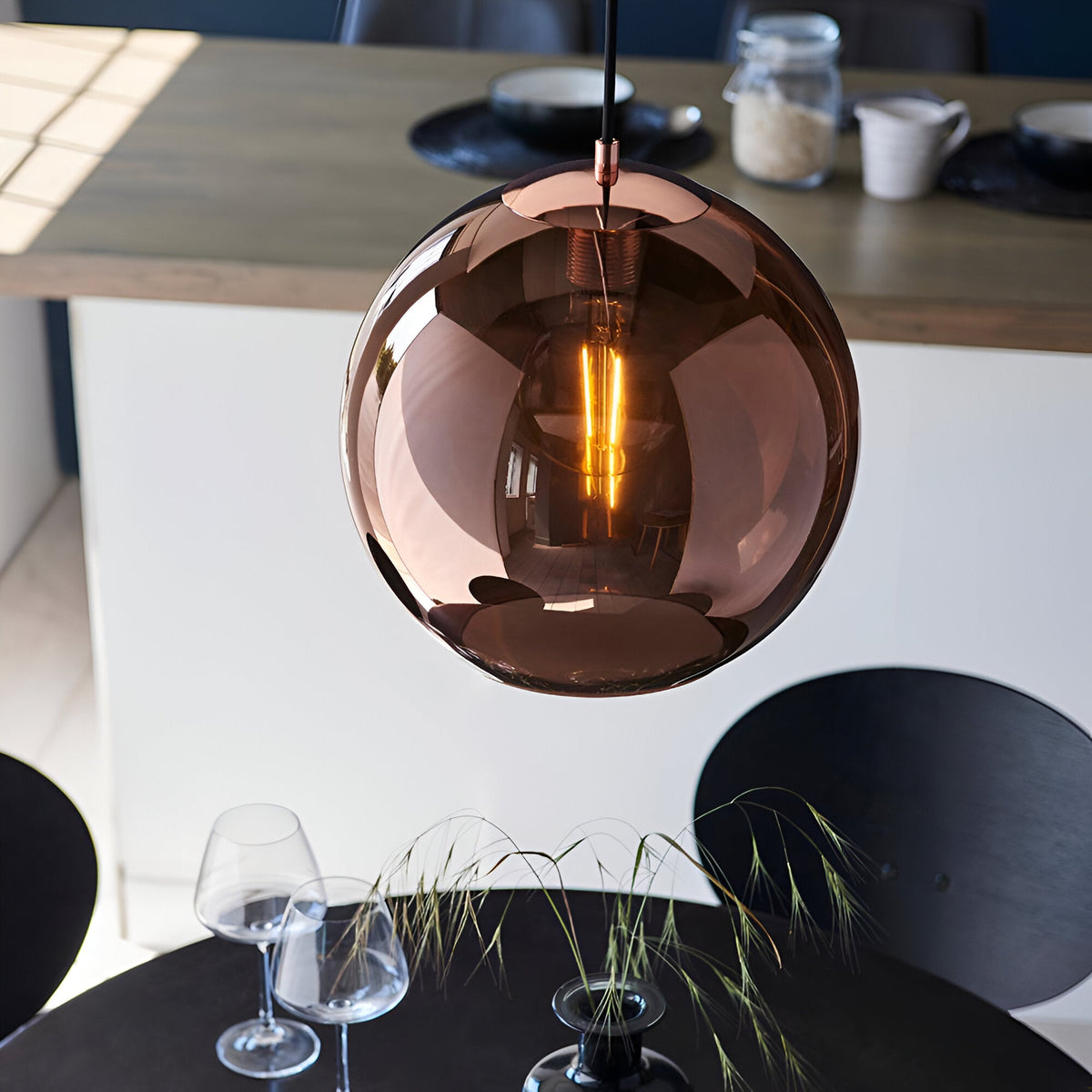 Endon Ashbourne pendant with a copper mirrored glass globe shade and black cable, lit above a dining table with wine glasses and grasses.