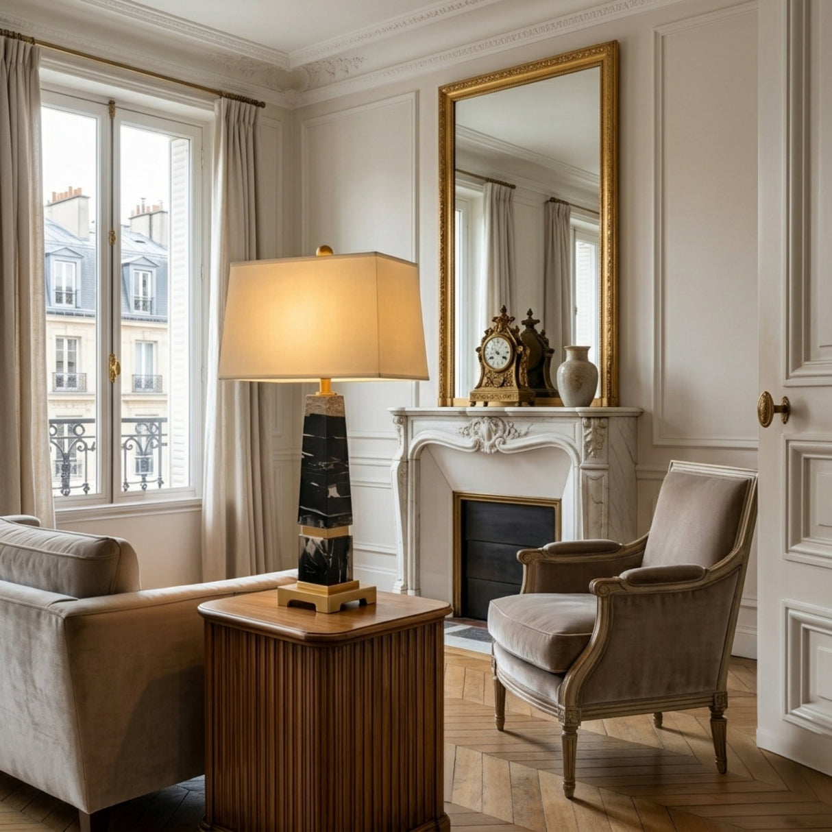 Elegant living room with a classic armchair, sofa, and the Aurevon 1 Light Tapered Marble Table Lamp in Brass & Black beside a wooden table. Features include a decorative fireplace, gold-framed mirror, clock, vases, large windows, and parquet flooring.