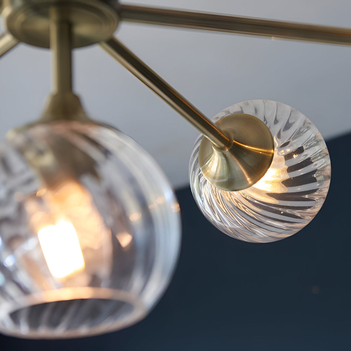 Close-up of Endon Georgiana 8 light semi-flush pendant showing brass arms and spiral-cut clear glass globe shades with lit E14 lamps.