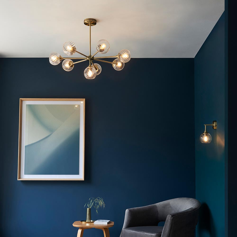 Georgiana Wall Light in brass with spiral-patterned glass globe shade, mounted on a dark blue wall in a living room setting.