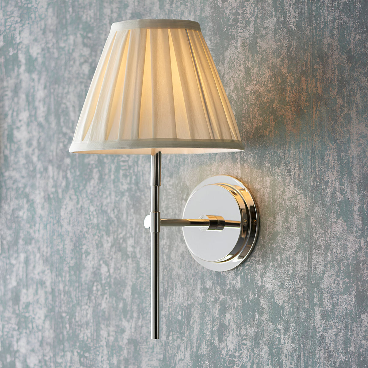Endon Chartwell wall light with pleated cream cotton tapered shade and polished nickel bracket, mounted on a distressed blue-grey wall.