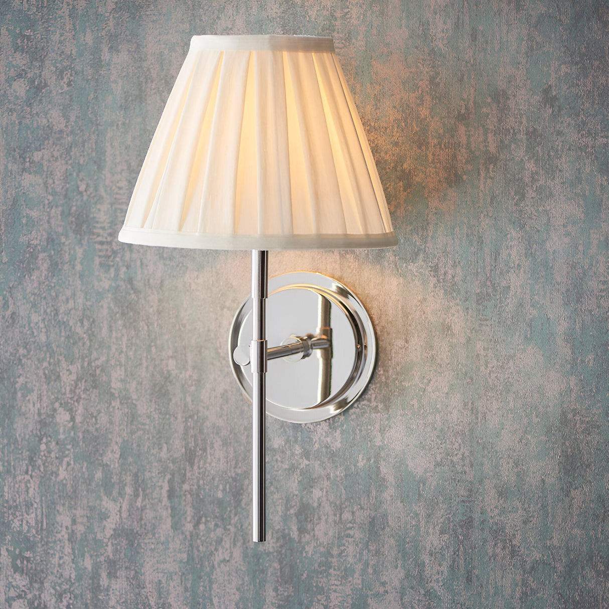 Endon Chartwell wall light with tapered cream box-pleat cotton shade and nickel bracket, mounted on a textured grey-green wall.