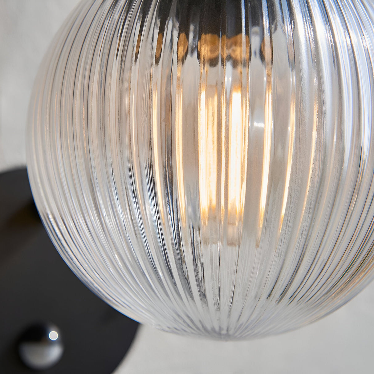 Close-up of the Endon Brackgrove outdoor wall light showing its clear ribbed glass globe shade illuminated by a filament bulb against a black fitting.