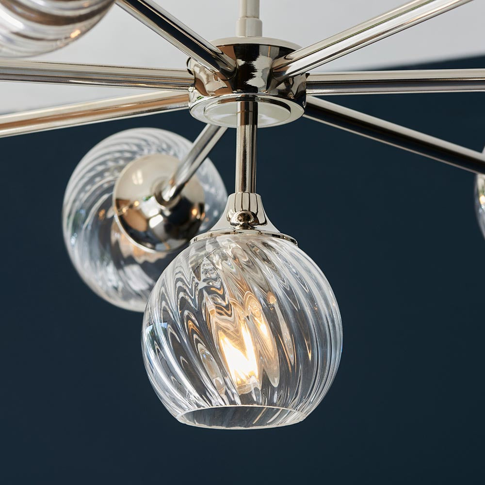 Endon Georgiana 8 light pendant close-up showing nickel-plated frame and spiral-cut clear glass globe shades with a lit E14 lamp against a dark blue backdrop.