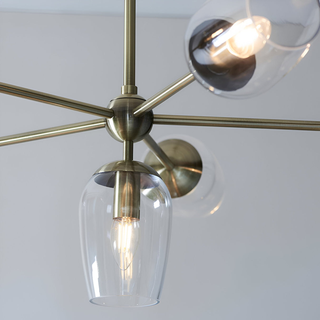 Close-up of the Caldworth 6 Light Pendant in brass, showing curved metal arms, a central sphere joint, and clear glass shades with visible E14 bulbs.