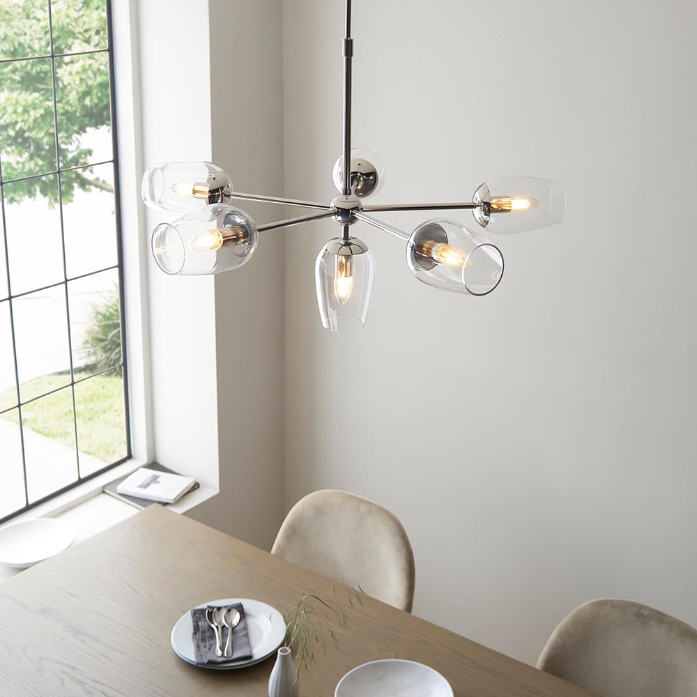 Endon Caldworth 6 Light Pendant in nickel with slender curved arms and clear blown glass shades, shown above a dining table beside a tall window.