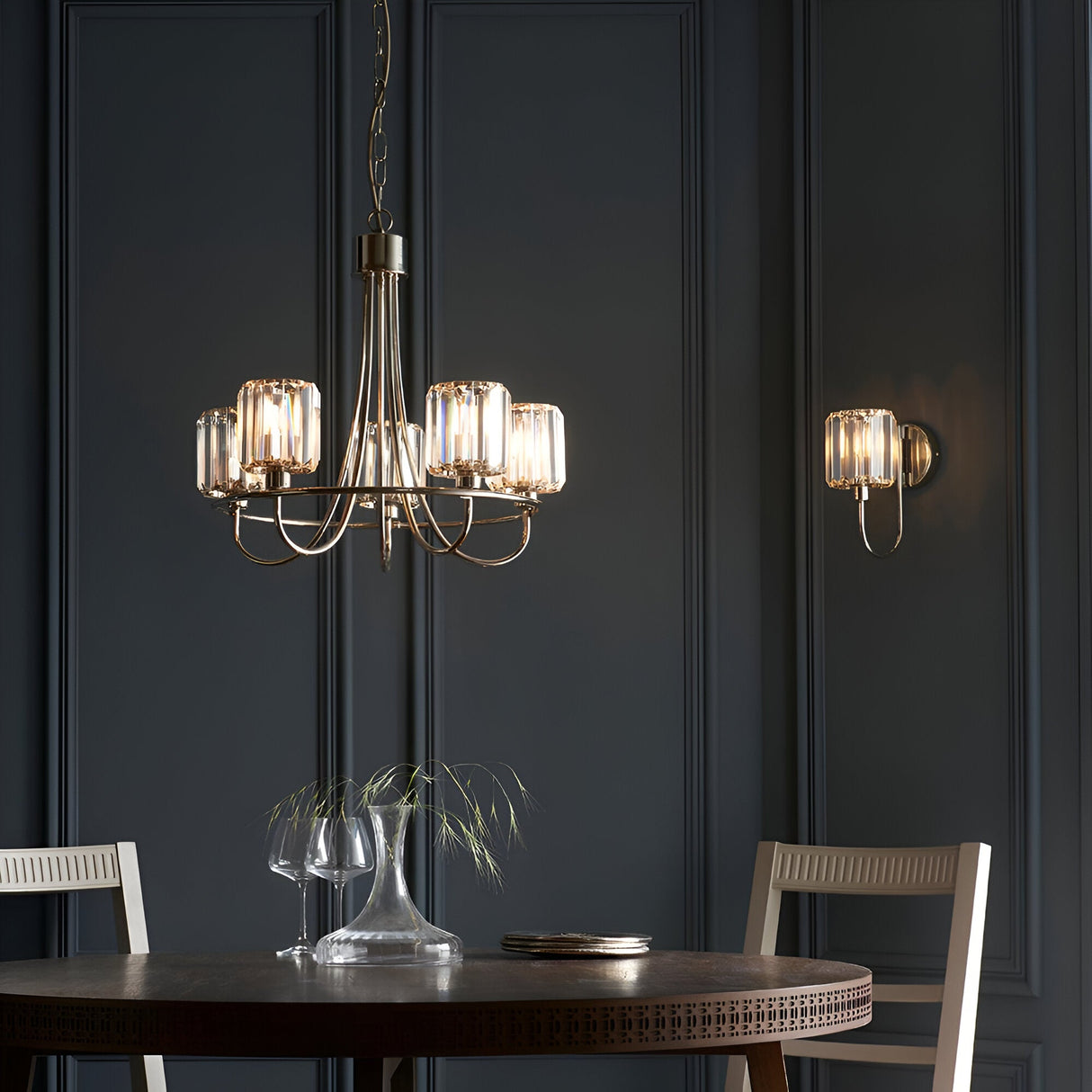 Clementine 5 Light Pendant in nickel with faceted glass shades on curved arms, hung above a dining table in a dark panelled room.