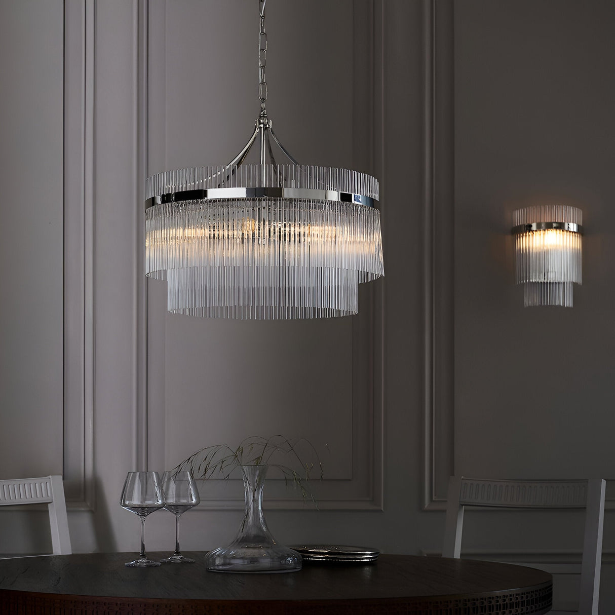 Beaumont 5 Light Pendant in nickel with two-tier clear glass rod shade, hung from a chain above a dining table in a grey panelled room.