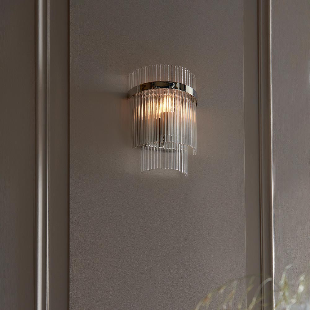 Endon Beaumont wall light in nickel with curved clear glass rods and lit E14 bulb, mounted on a panelled neutral wall.