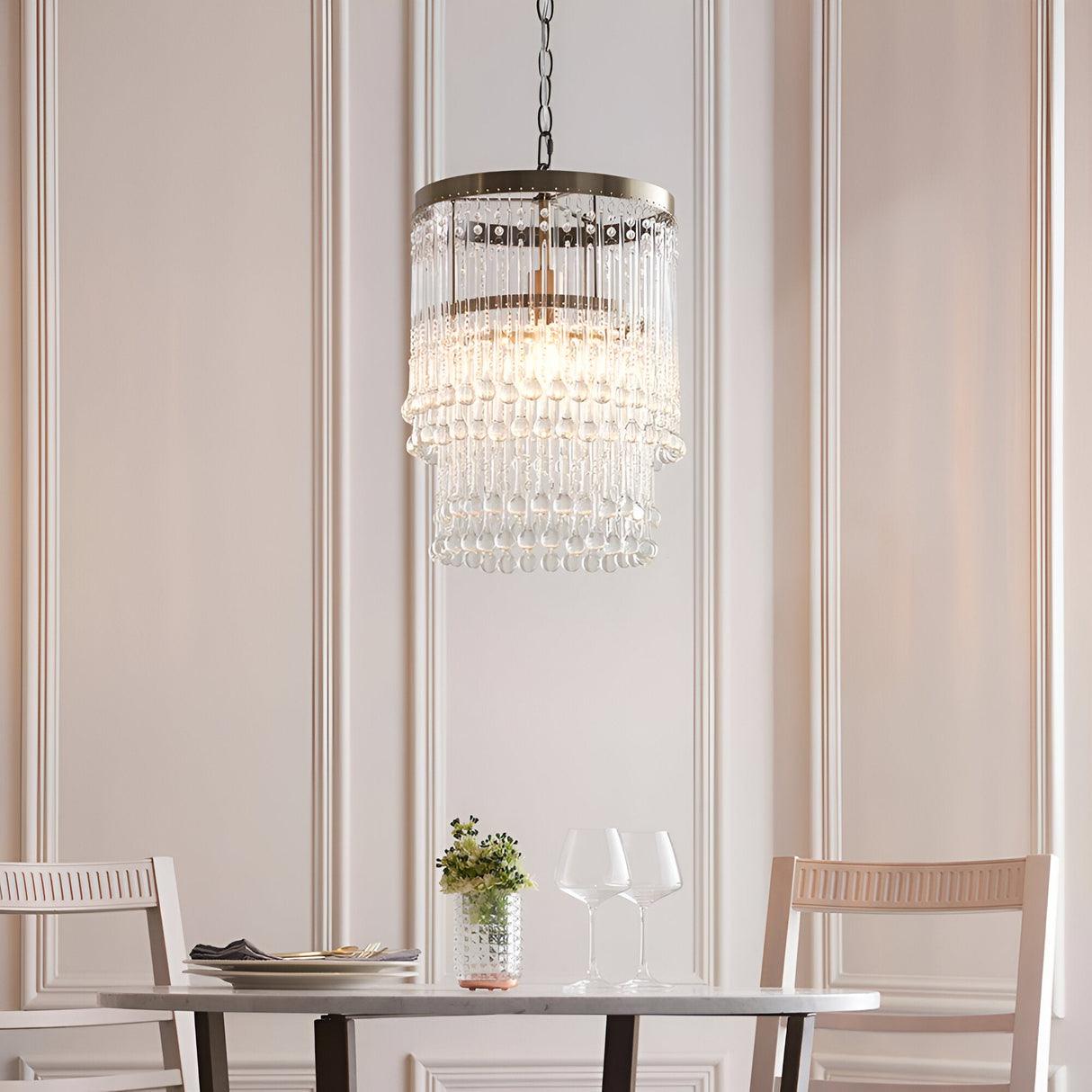 Bramgrove Pendant in antique brass with tiered clear glass droplets, hung above a dining table in a soft pink-toned room.