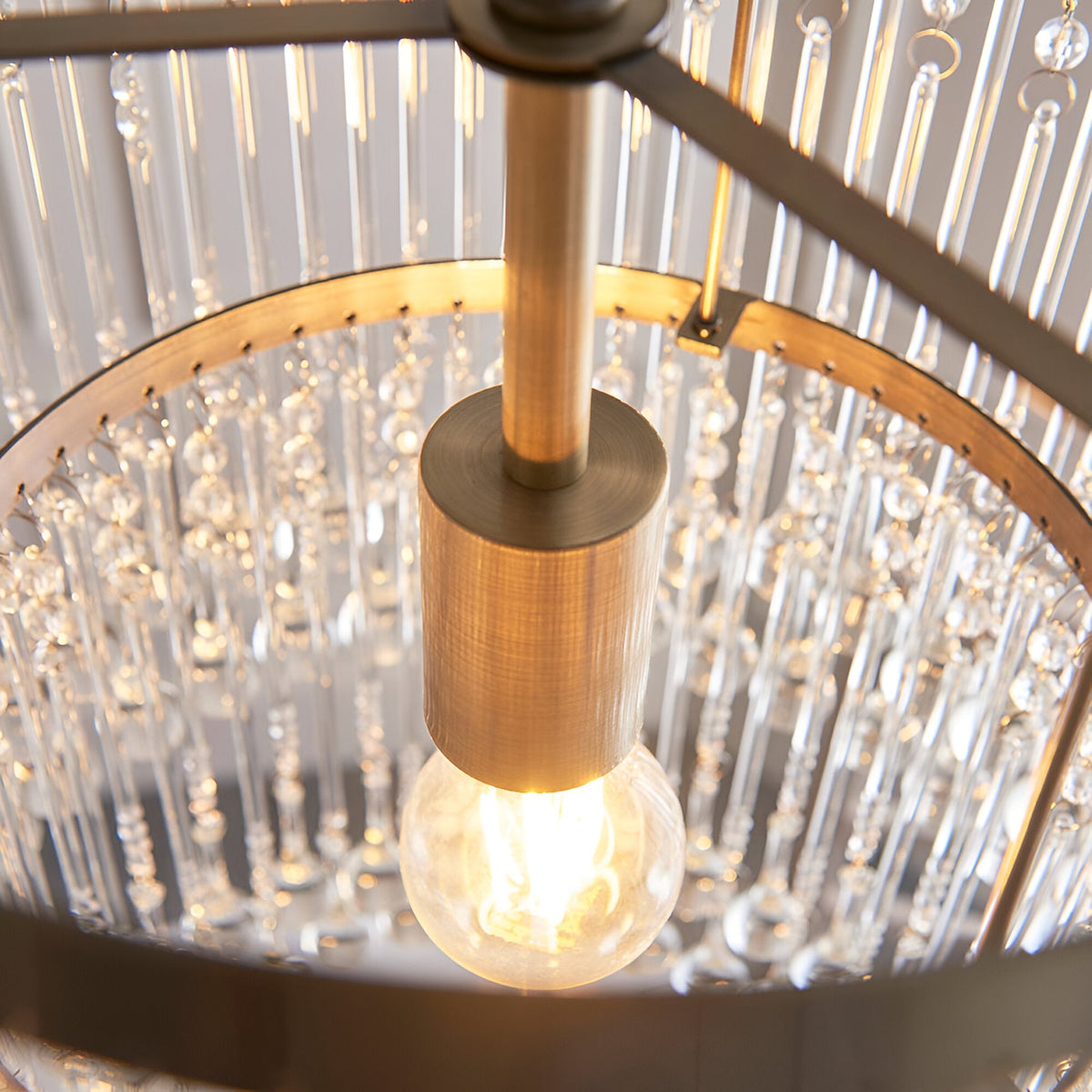Close-up of the Bramgrove Pendant in antique brass, showing the E27 bulb holder and glass droplet strands catching the light.