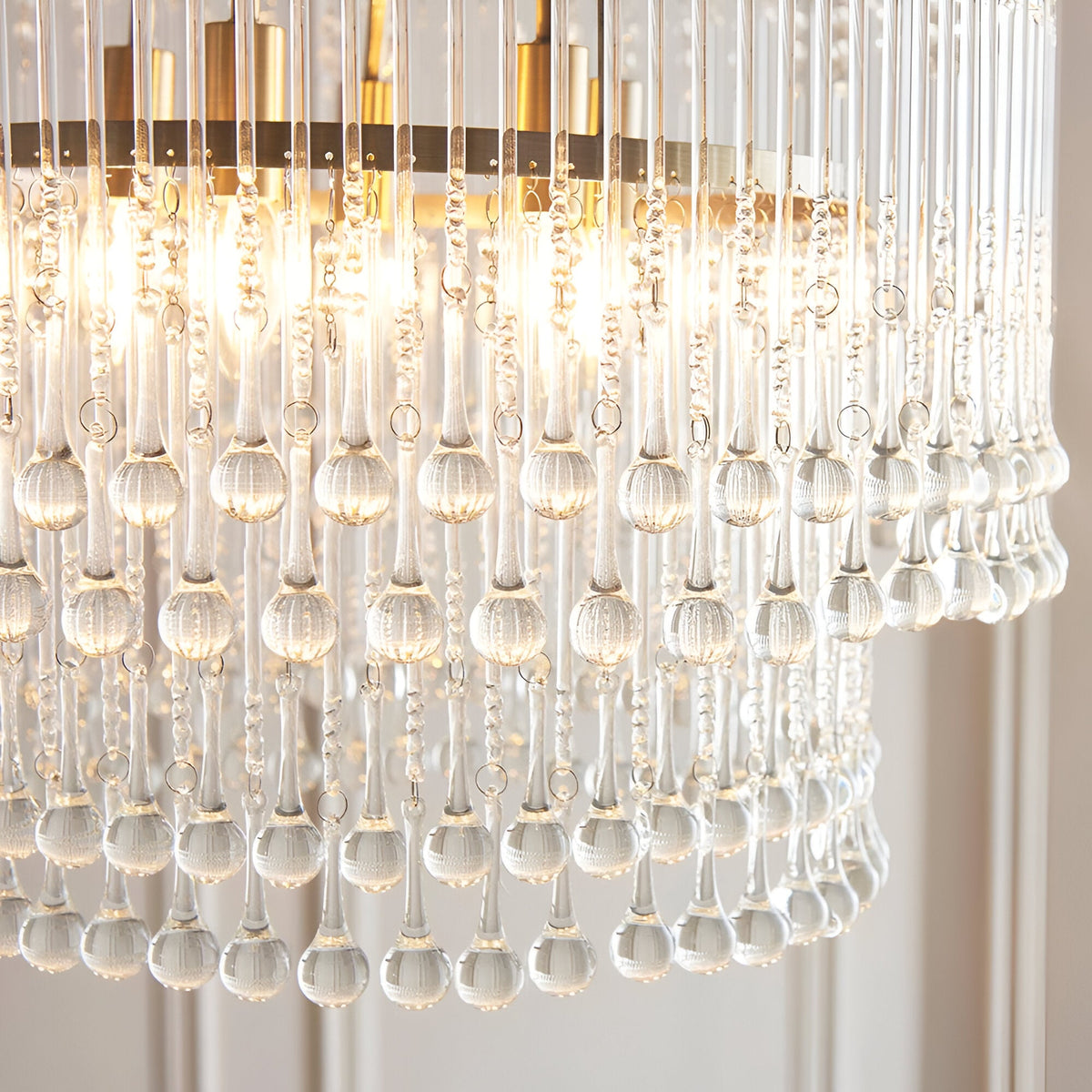 Close-up of Endon Bramgrove 5 Light Pendant in antique brass, showing tiered clear glass droplets and lit E14 lamps within the frame.