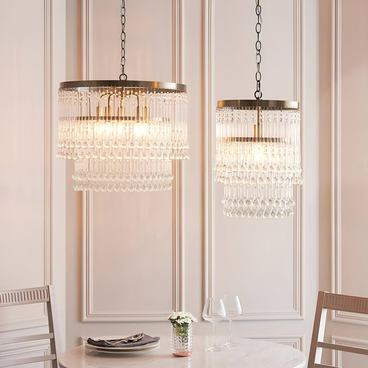 Endon Bramgrove pendant lights with tiered clear glass droplets on antique brass frames, shown in two sizes above a dining table setting.